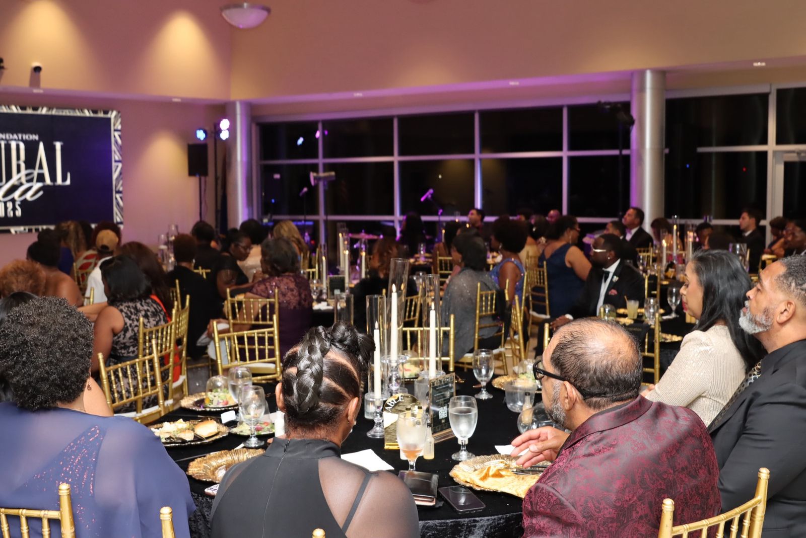 Guests seated at round tables under purple lighting at the Foundation’s 2025 Inaugural Gala, the event banner at the far end of the room.
