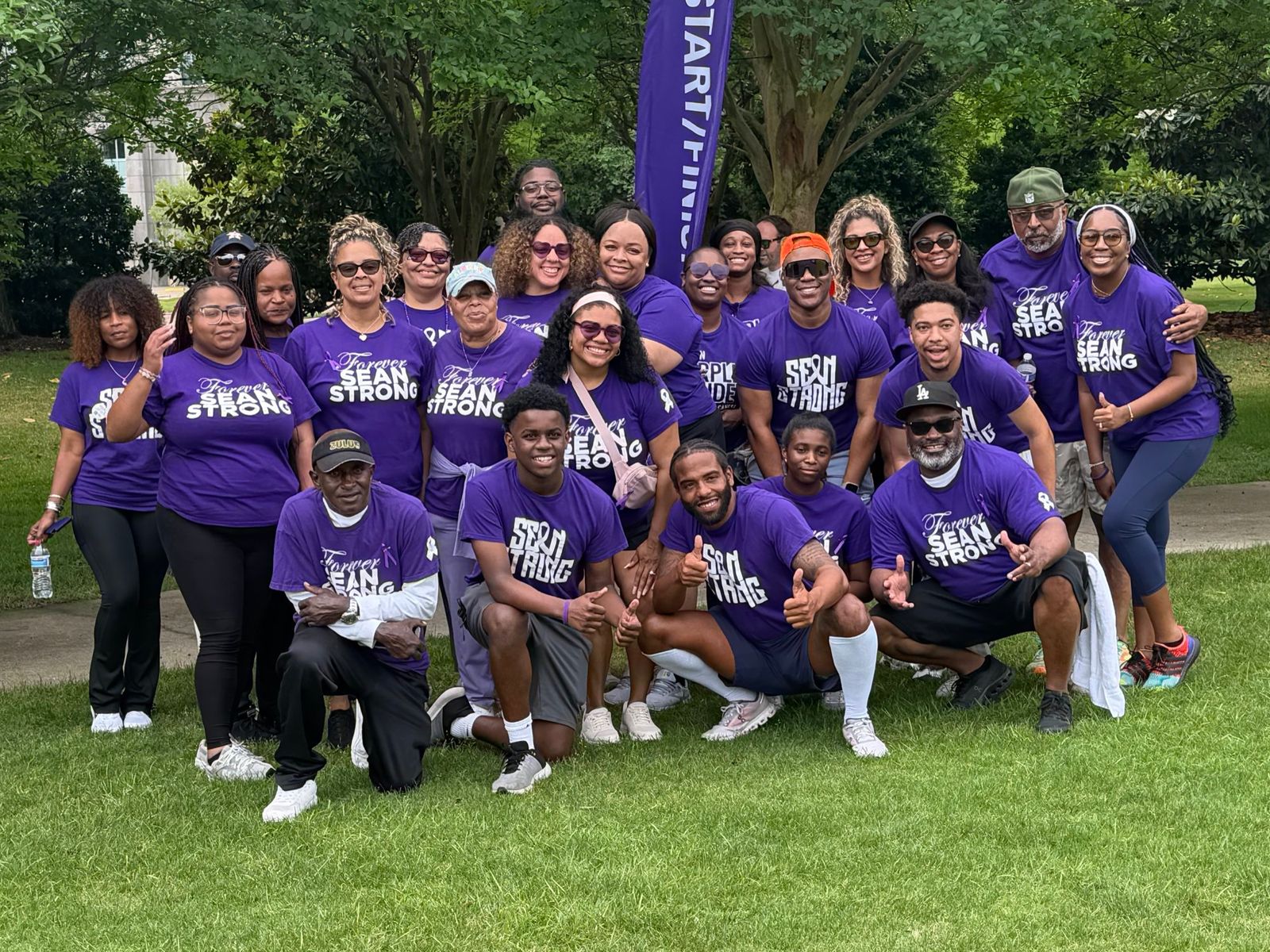 Team Sean Strong on a lawn at PurpleStride, in purple “Forever Sean Strong” shirts beneath a start and finish banner.