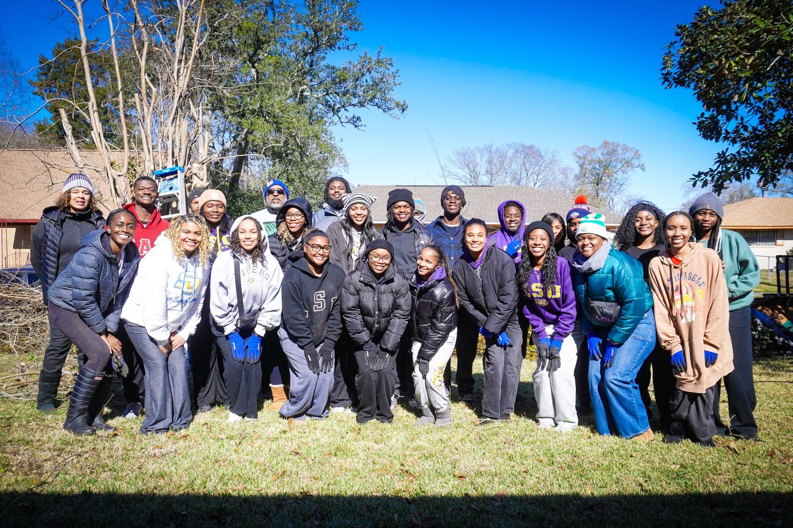 A large group of volunteers in winter coats, gathered for a group photograph on a lawn outside a house.